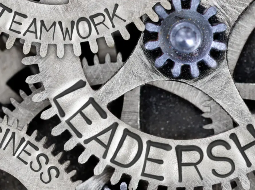 Close-up of interlocking metal gears labeled with words like "Leadership," "Teamwork," "Success," "Growth," "Business," and "Company" to symbolize synergy in organizational leadership and strategy.