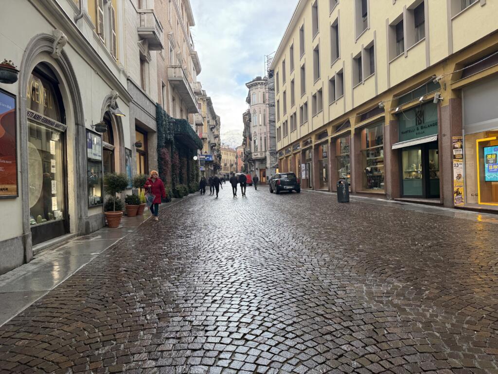 Cobblestone street in Biella, Italy with pedestrians walking toward the Alps